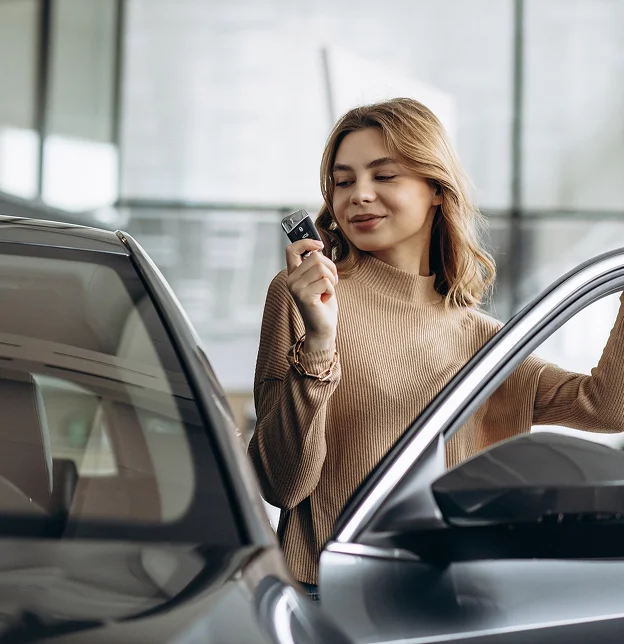 Femme souriante avec une clé de voiture devant une nouvelle voiture.