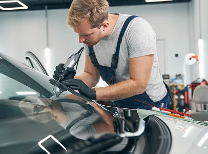 Homme réparant un pare-brise de voiture avec un outil électrique à Brou en Eure-et-Loir 28