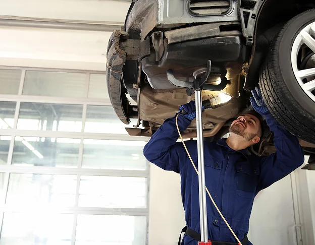 Mécanicien réparant le dessous d'une voiture surélevée avec une lampe torche à Brou en Eure-et-Loir 28