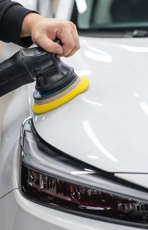 Main polissant le capot blanc d'une voiture avec une polisseuse orbitale à Brou en Eure-et-Loir 28
